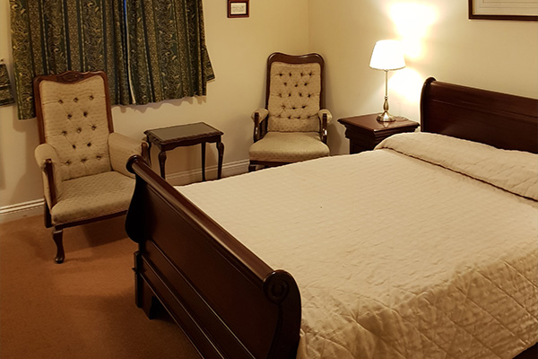 cozy bedroom with wooden furniture and two chairs featuring a bedside lamp and curtains offering a serene atmosphere suitable for restful stays and perfect for seven guests