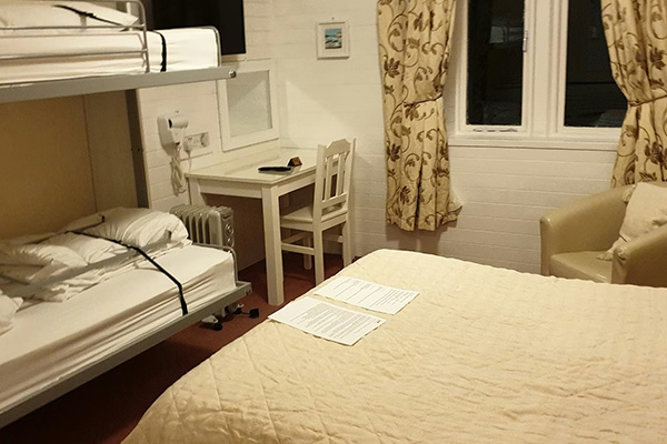 a cozy hotel room featuring a double bed with a quilt a bunk bed with pillows a small desk and chair and curtain windows ideal for four travelers