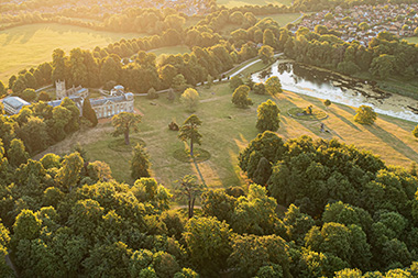 aerial view of a lush green landscape featuring trees and a serene river with a historical building in the background perfect for exploring nature's beauty in twelve ways