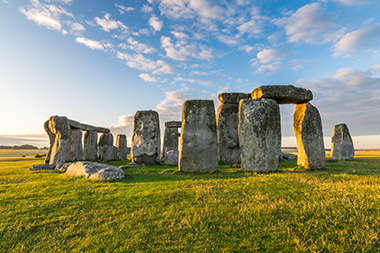 ancient stone structure at Stonehenge under blue sky surrounded by green grass 15 historical sites in the UK