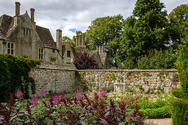 historic garden with flowering plants and stone wall behind traditional architecture surrounded by trees 14th century charm and beauty