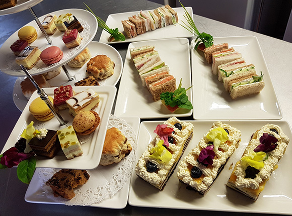 assorted desserts and sandwiches displayed on plates colorful macarons scones and pastries afternoon tea selection three tiered stand