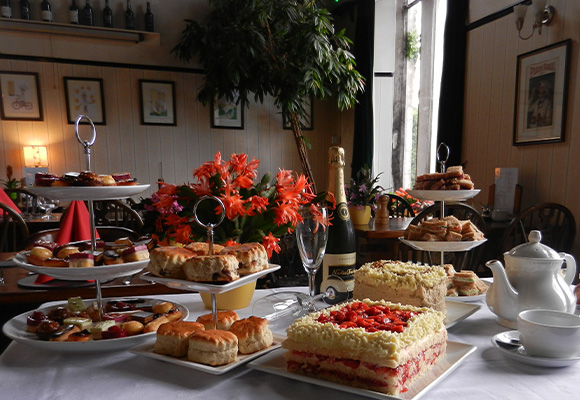 a beautifully arranged table with various pastries cakes and scones surrounded by flowers and champagne ideal for a delightful afternoon tea experience