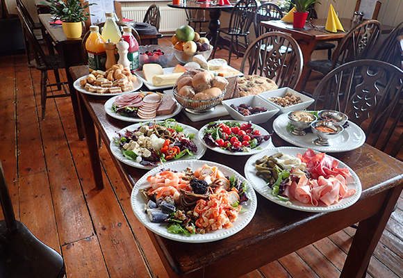 various plates of food including salads seafood meats and snacks on a wooden table in a dining area with drinks in the background perfect for two gatherings