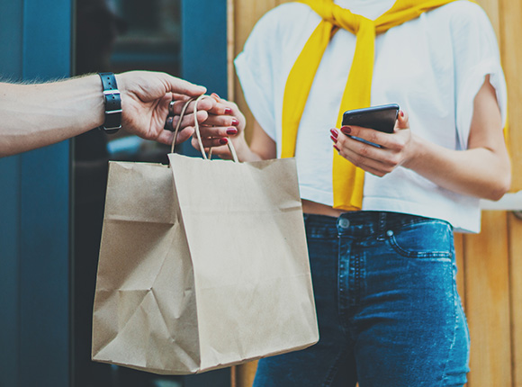 person receiving a brown paper bag while using a smartphone wearing a stylish outfit and a yellow scarf 3 shopping options available